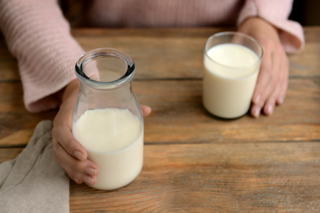 Woman with bottle and glass of fresh milk at wooden tableの写真素材