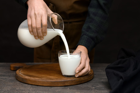 Woman pouring fresh milk from jug into glass on tableの写真素材