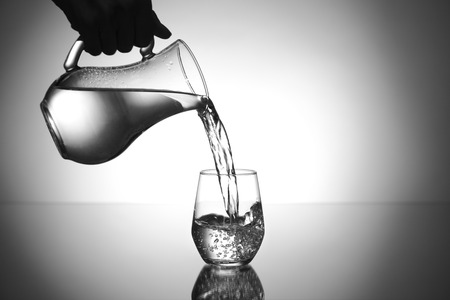 Pouring of water from jug into glass on tableの写真素材