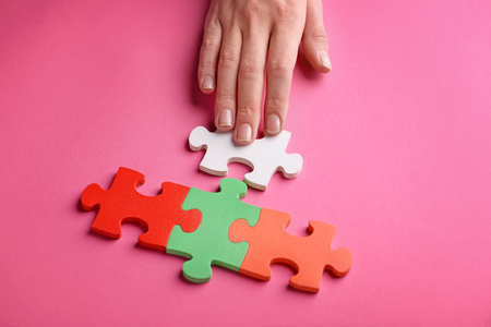Female's hand with pieces of puzzle on color backgroundの写真素材