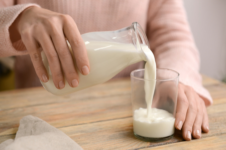 Woman pouring fresh milk from bottle into glass on wooden tableの写真素材