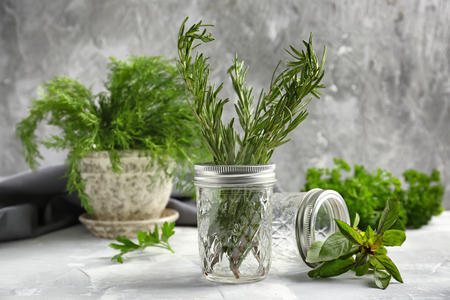 Jars with fresh aromatic herbs on light tableの写真素材