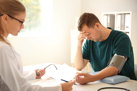 Female doctor measuring blood pressure of male patient in hospitalの写真素材