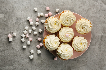 Plate with sweet cupcakes and marshmallows on grey tableの写真素材