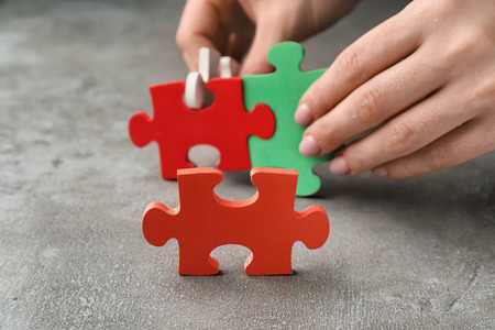 Female hands with pieces of puzzle on grey backgroundの写真素材