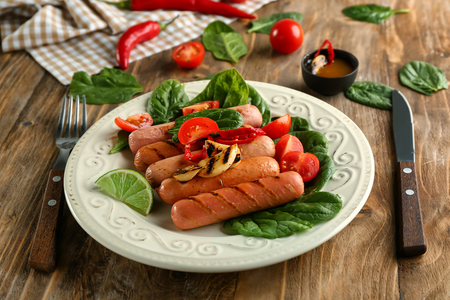 Plate with delicious grilled sausages and vegetables on wooden tableの写真素材
