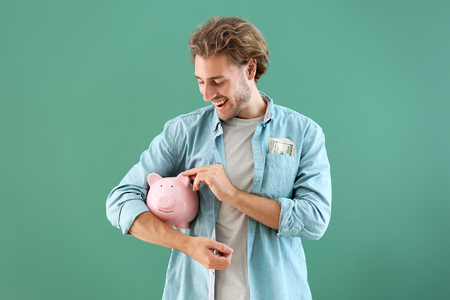 Handsome man with piggy bank on color backgroundの写真素材