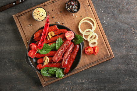 Frying pan with delicious roasted sausages and vegetables on tableの写真素材