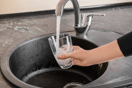 Woman filling glass with water from faucetの写真素材