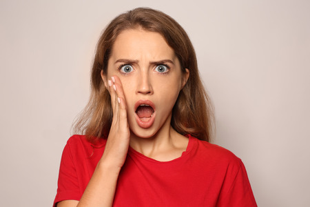 Portrait of shocked young woman on light backgroundの写真素材