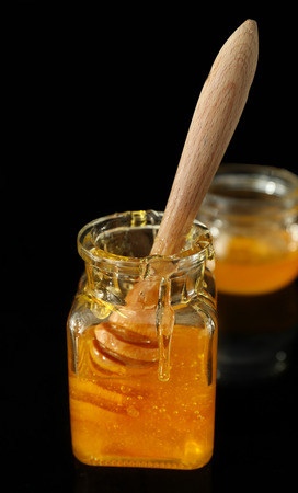 Wooden dipper in jar with honey against dark backgroundの写真素材
