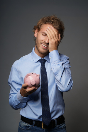 Upset man with piggy bank on grey backgroundの写真素材