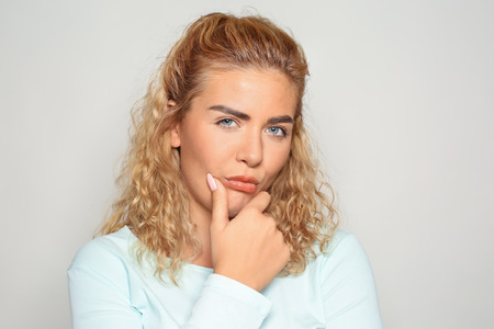 Portrait of mistrustful young woman on light backgroundの写真素材