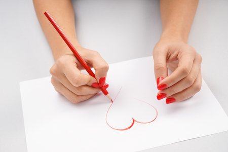 Woman drawing heart on sheet of paperの写真素材
