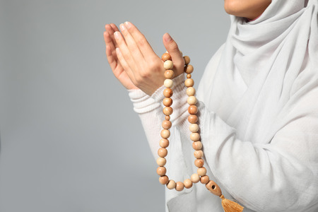 Young Muslim woman with rosary beads praying on light background, closeupの写真素材
