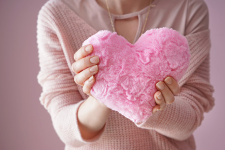 Woman holding fluffy heart-shaped pillow on color background, closeupの写真素材