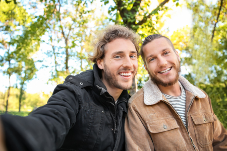 Happy gay couple taking selfie in parkの写真素材