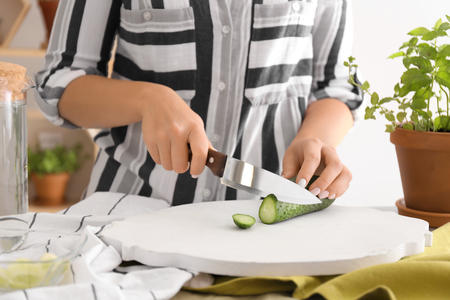 Woman cutting fresh cucumber on wooden boardの写真素材