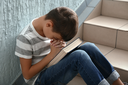 Little boy with Bible praying on stairsの写真素材