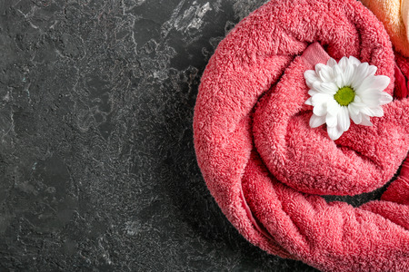 Rolled clean towel with beautiful flower on grey textured background, top viewの写真素材
