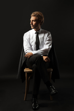 Handsome businessman sitting on chair against black backgroundの写真素材