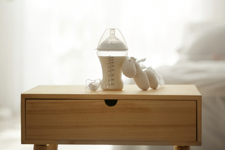 Feeding bottle with milk, soother and toy on table in light roomの写真素材