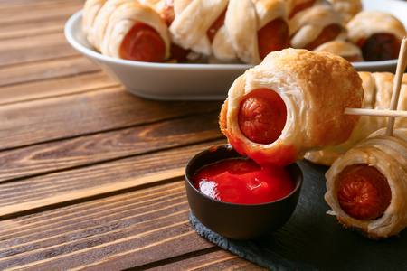 Delicious sausage rolls with bowl of ketchup on wooden tableの写真素材