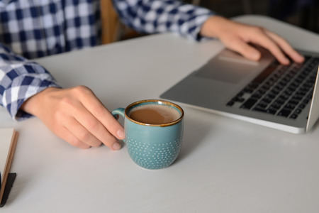 Woman drinking aromatic coffee while using laptop at tableの写真素材