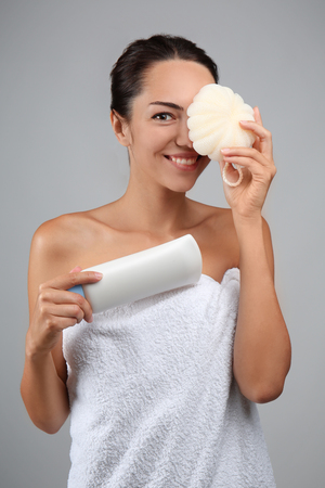 Beautiful young woman with shower sponge and shampoo on grey backgroundの写真素材