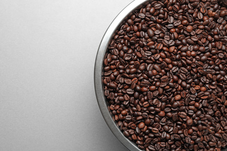 Metal bowl with coffee beans on light background