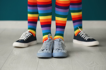 Legs of young lesbian couple in rainbow stockings standing against color wallの写真素材