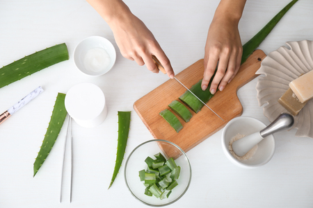 Female's hands cutting aloe leaf on wooden board, top viewの写真素材