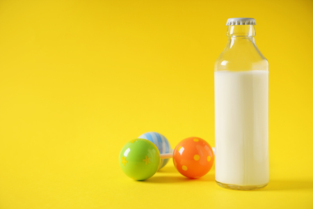 Bottle of milk and rattle on color backgroundの写真素材