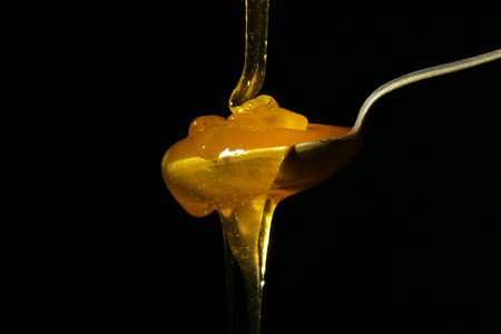 Honey pouring in spoon against dark backgroundの写真素材