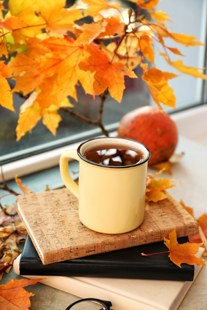 Metal cup of aromatic tea with autumn leaves on windowsillの写真素材