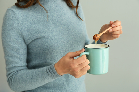Woman adding honey into mug of milk on grey background, closeupの写真素材