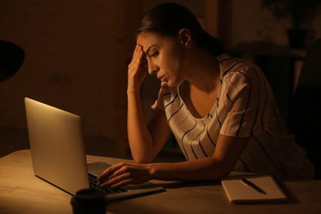 Woman suffering from headache while working with laptop late in eveningの写真素材