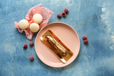 Plate with tasty eclair and macarons on color table