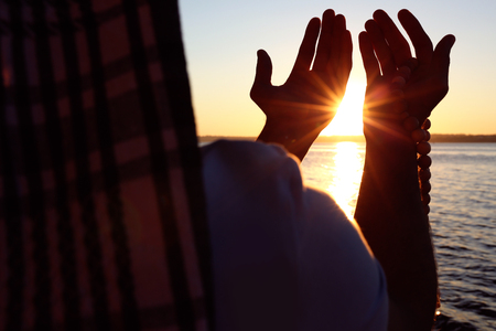 Young Muslim man praying near river at sunsetの写真素材