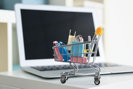 Small cart and laptop on table. Internet shopping concept