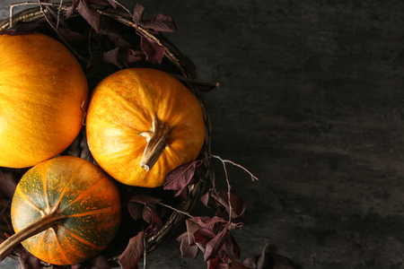 Wicker bowl with whole fresh pumpkins and autumn leaves on dark tableの写真素材
