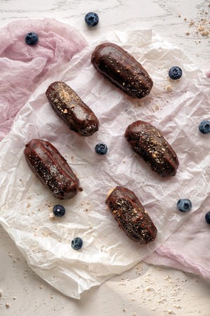 Tasty eclairs with blueberries on parchment