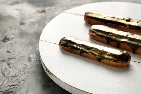 Wooden board with tasty eclairs on grey table