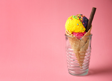 Waffle cone with delicious ice cream in glass on color backgroundの写真素材