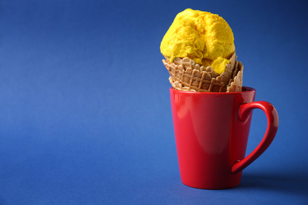 Waffle cone with delicious ice cream in cup on color backgroundの写真素材