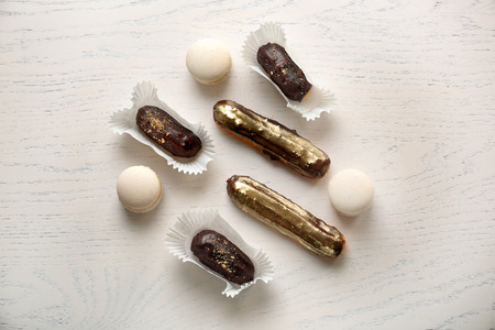 Tasty eclairs with macarons on white table