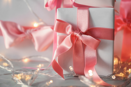 Gift box with pink ribbon and fairy lights on tableの写真素材