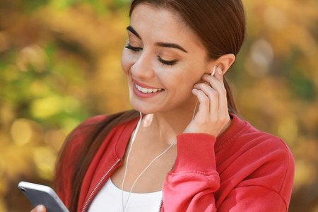 Sporty woman listening to music in autumn parkの写真素材
