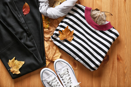 Stylish outfit with shoes and autumn leaves on wooden background, top viewの写真素材