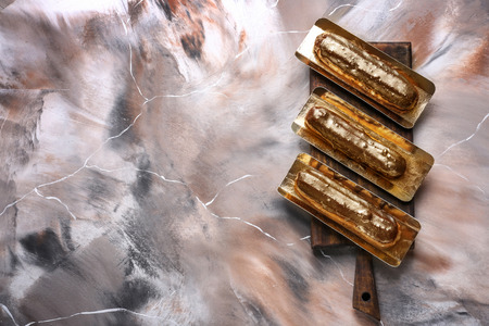 Wooden board with delicious eclairs on marble table